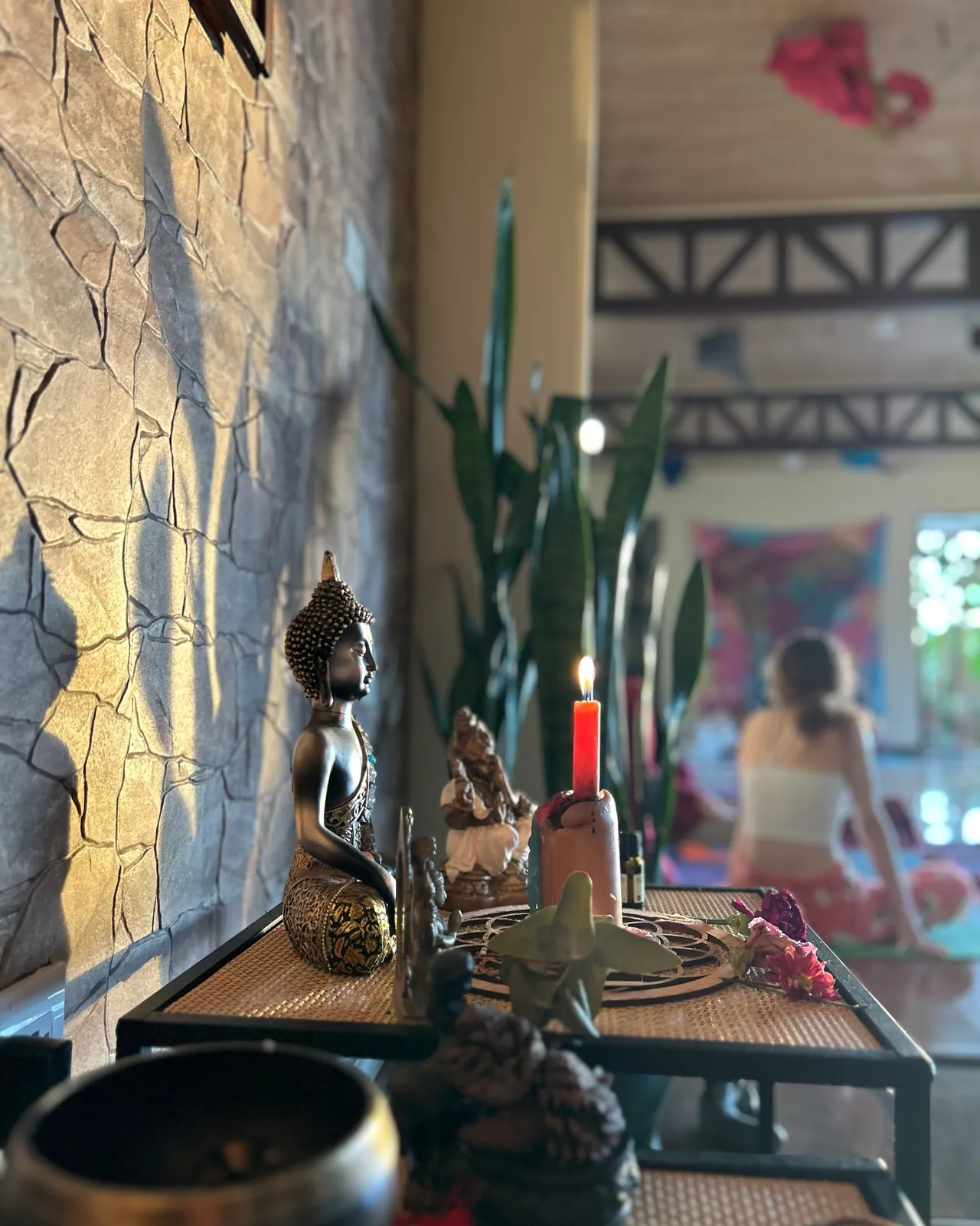 El altar de la casa con un Buda, una vela encendida y flores; al fondo, una clase