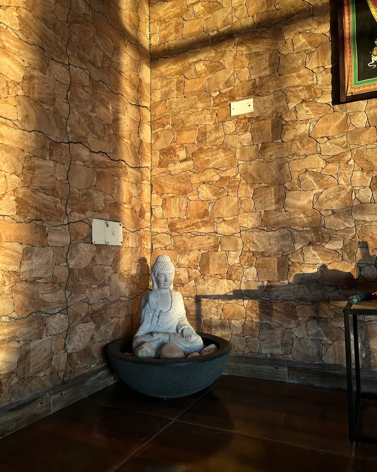 Un Buda de piedra en un rincón del salón, con la luz de la tarde sobre la pared