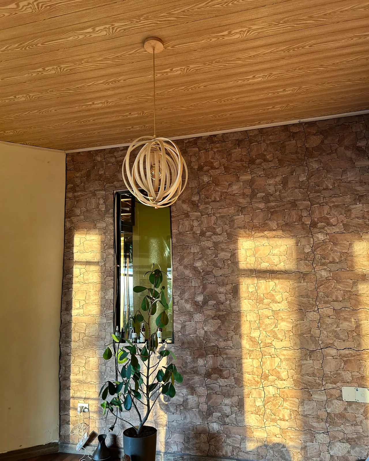 Una lámpara de fibras, una planta y la pared de piedra con la sombra de las ventanas