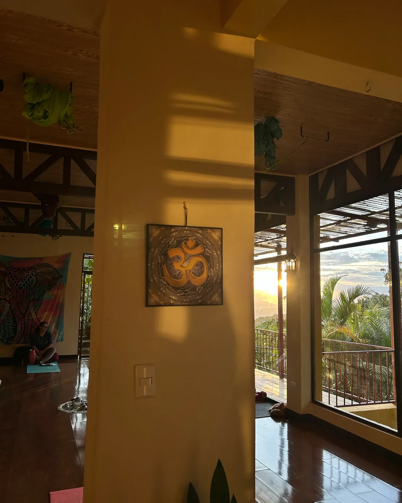 El símbolo Om en una columna del salón y, detrás, el sol poniéndose sobre las montañas