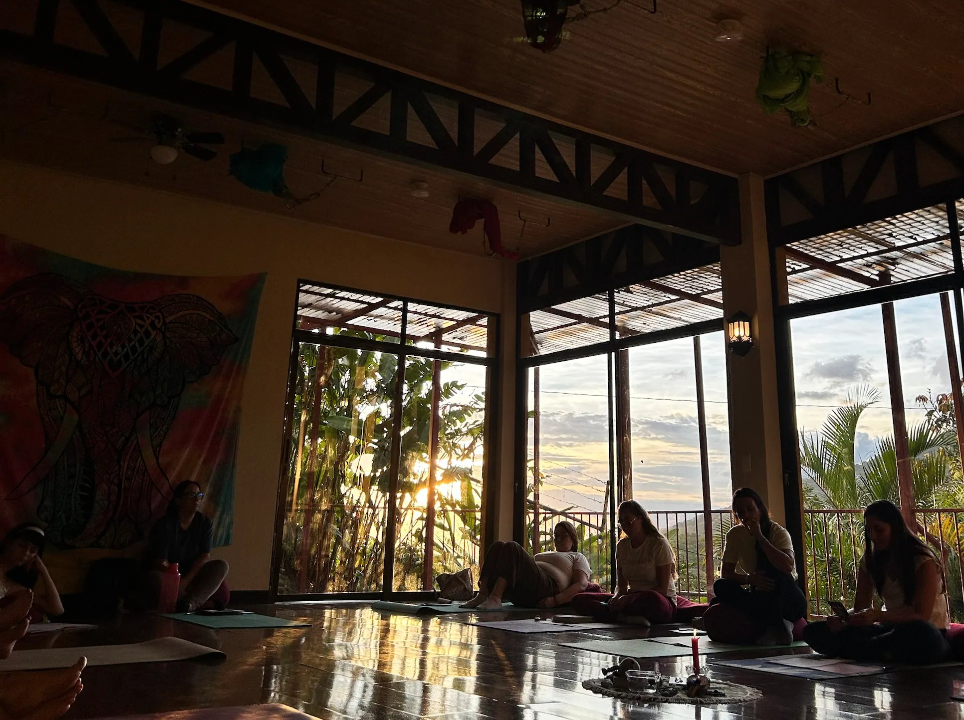 El salón de Casa Yoga+Surya al atardecer: ventanales abiertos a las montañas y el piso de madera reflejando la luz